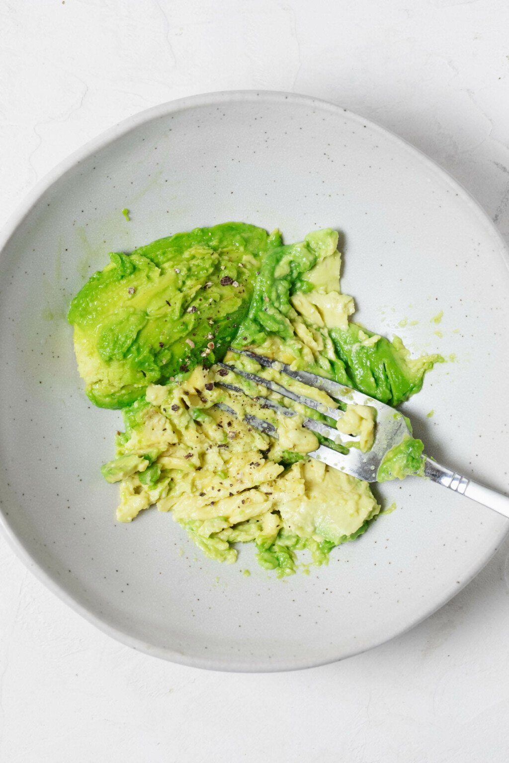 An image of a small white bowl, which is filled with bright green mashed avocado.