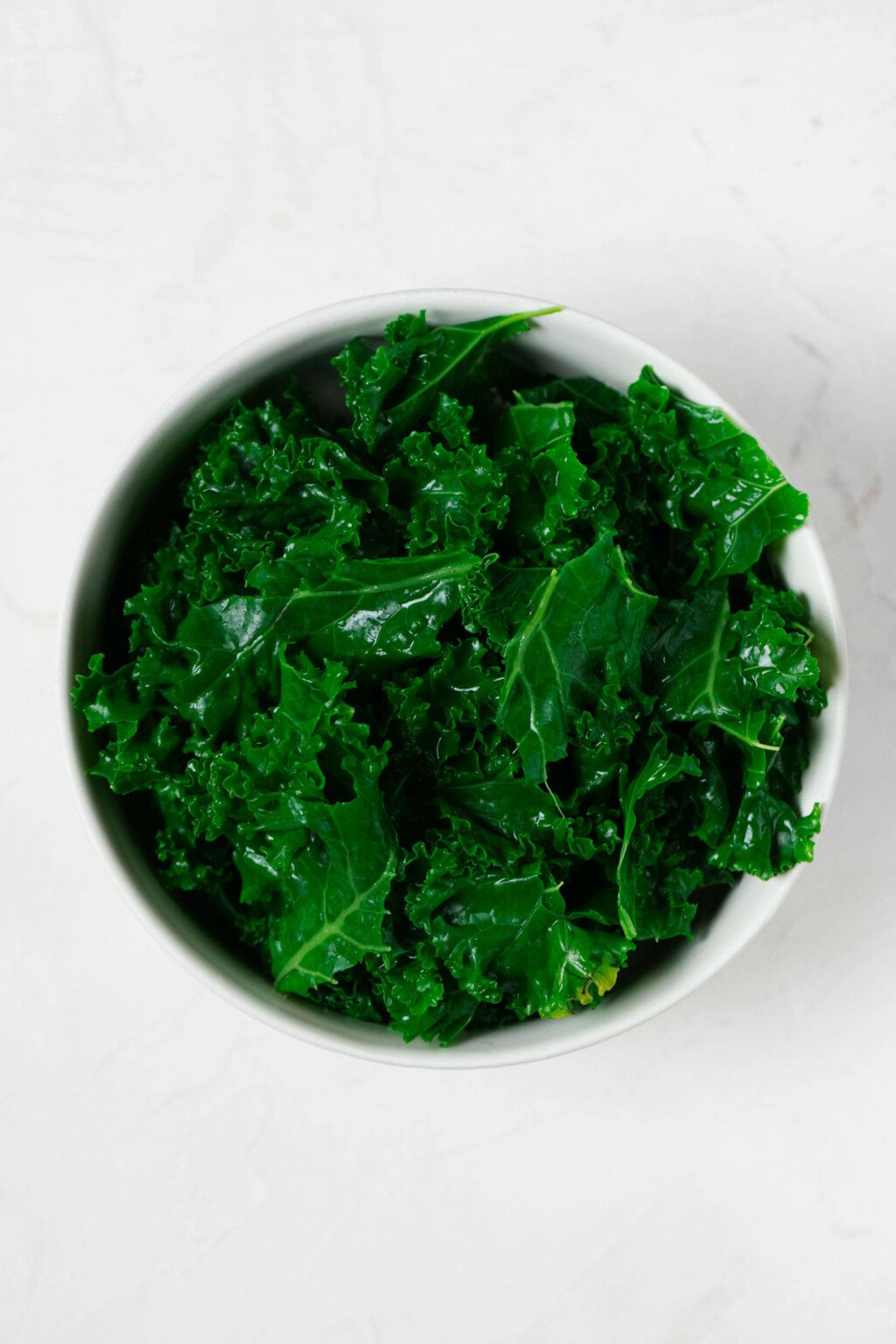 An overhead image of a small white bowl, filled with steamed kale. 