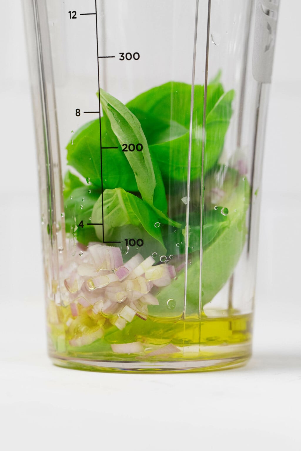 Basil, shallots, avocado, and oil are arranged in a small, personal-sized blender.