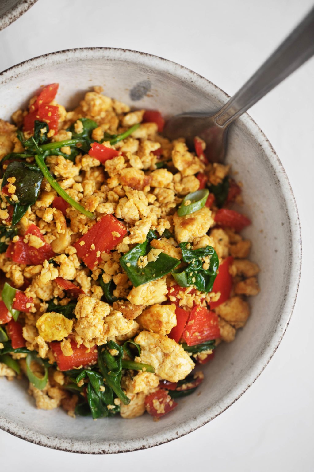 A close up shot of vegan classic tofu scramble, served with chopped green onions and wilted spinach.
