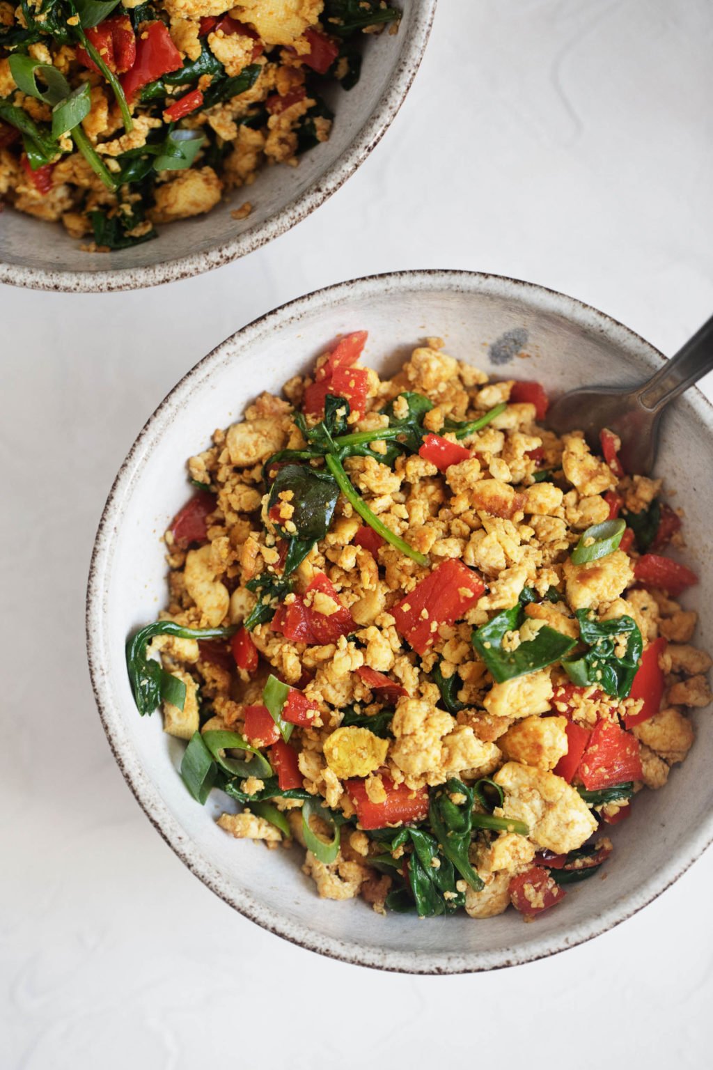 Two bowls of vegan classic tofu scramble, full of fresh vegetables and greens, ready to be served.
