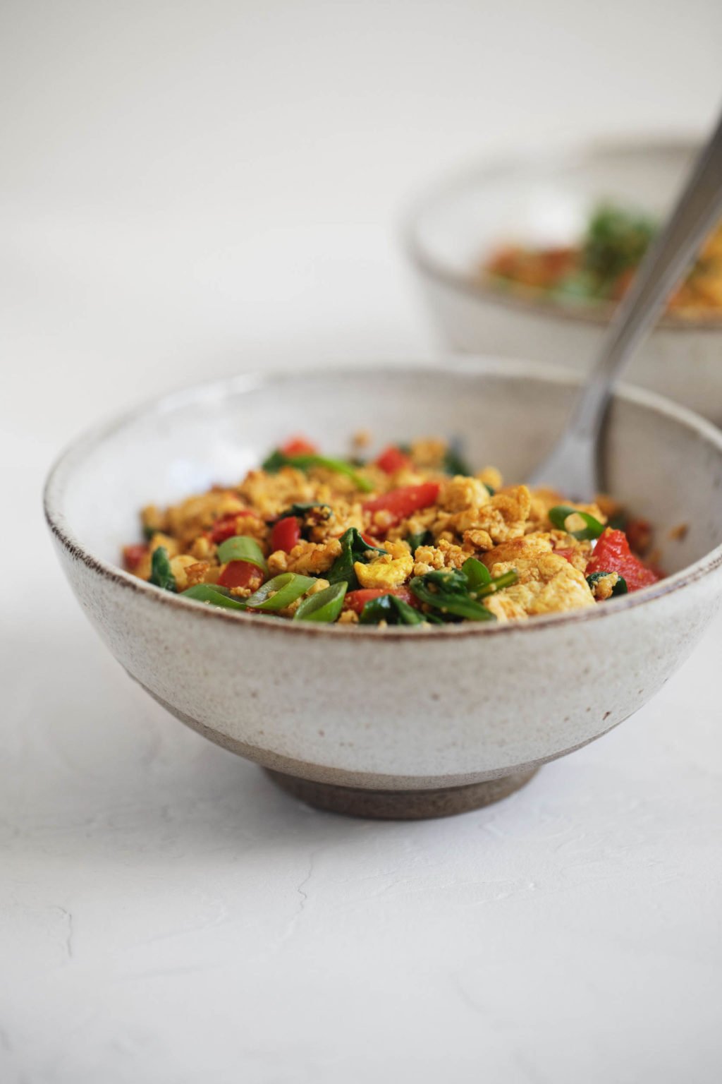 An angled shot of classic vegan tofu scramble, piled into two bowls with a serving spoon.