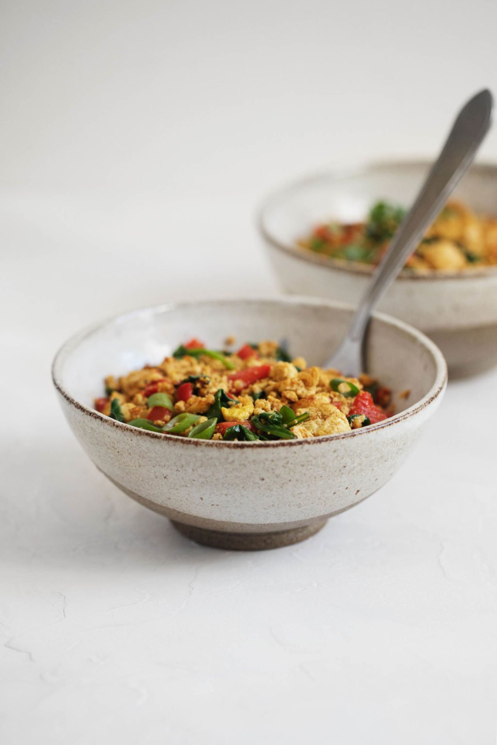 Two small bowls of a vegan scramble, made with tofu, vegetables, and seasonings.