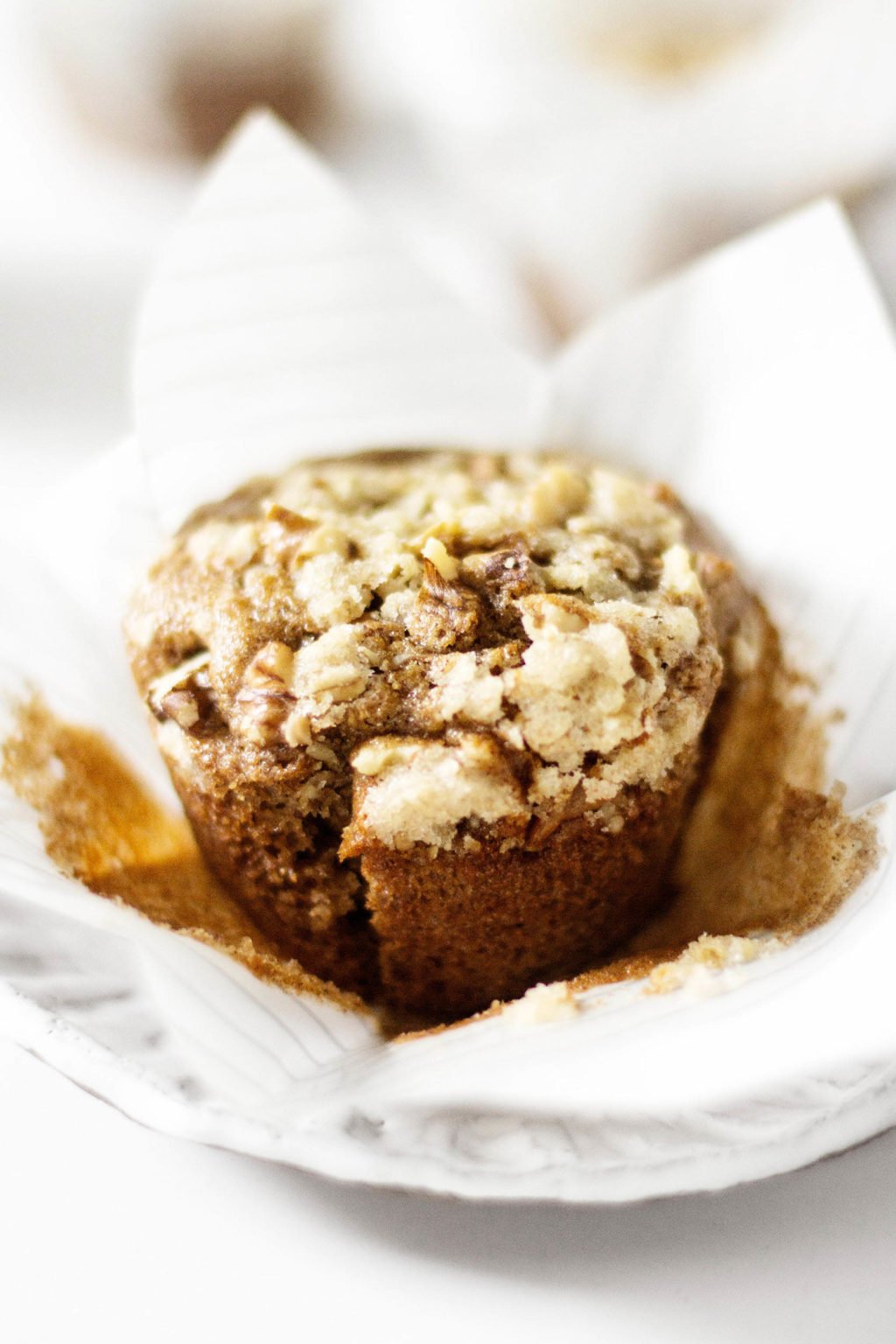 A vegan muffin is being held in a white paper liner. It rests on a white dessert plate.