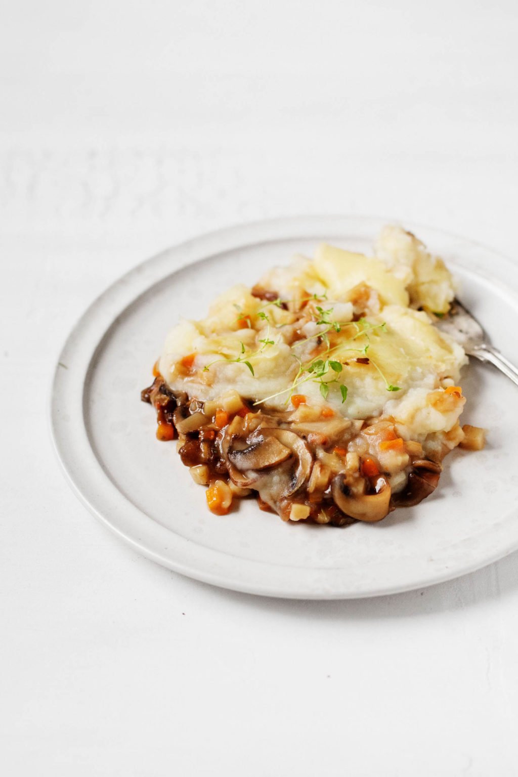 A vegan mushroom and vegetable shepherds pie, garnished with sprigs of herbs.