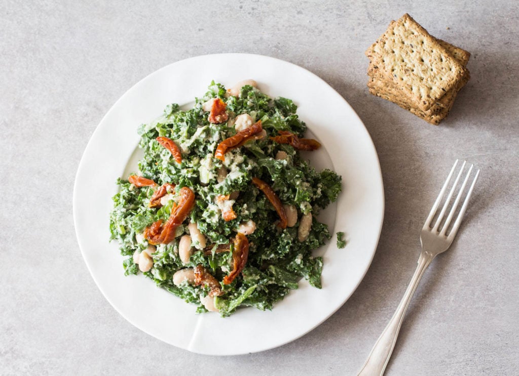 A nutritious, green salad is being served on a round, white plate with some crackers nearby.