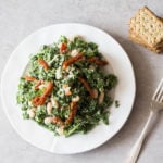 A nutritious, green salad is being served on a round, white plate with some crackers nearby.