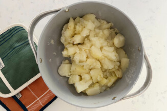 A gray pot holds cooked potato. There are colorful potholders nearby.