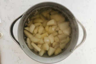 A gray pot is full of water and raw chunks of potato.