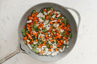 A gray pot holds onions, carrots, and celery before sautéing.
