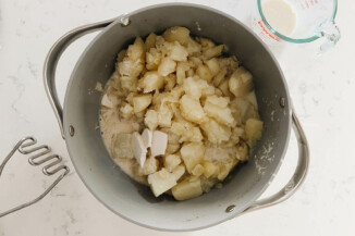 A gray pot is full of cooked potatoes, milk, and butter.