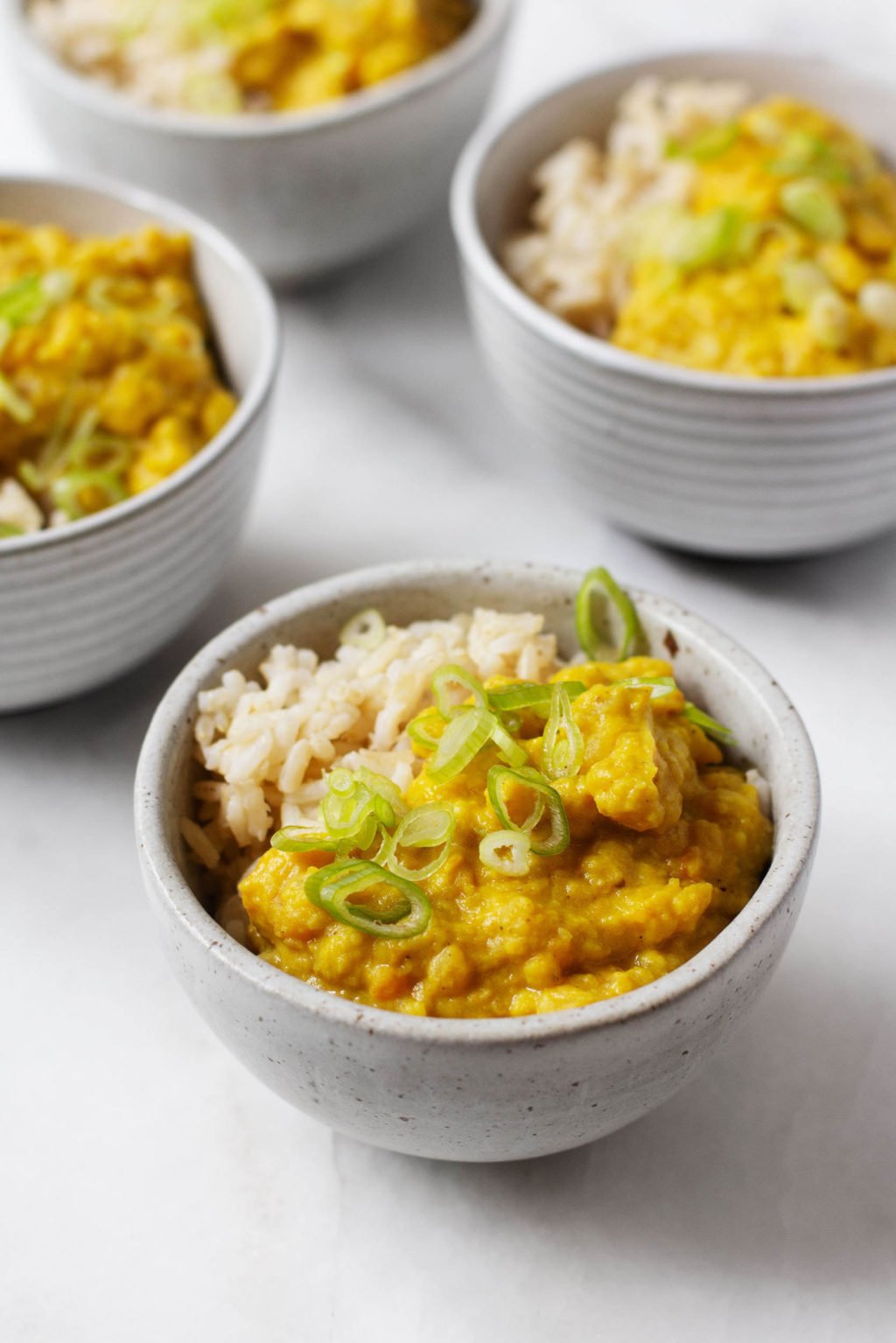 An angled photograph of a few bowls of golden vegan split pea coconut breakfast porridge, served with rice and topped with green onions.