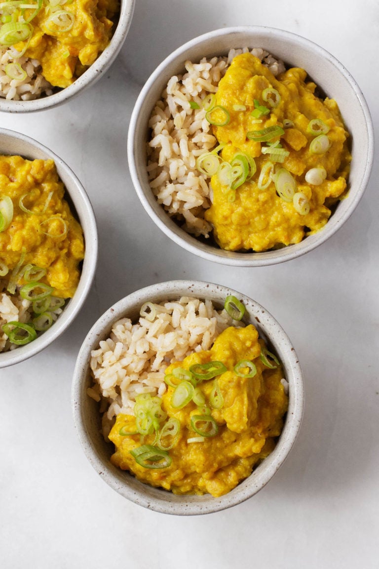 Four small bowls of a vegan split pea and coconut breakfast stew, served with rice and garnished with green onions.