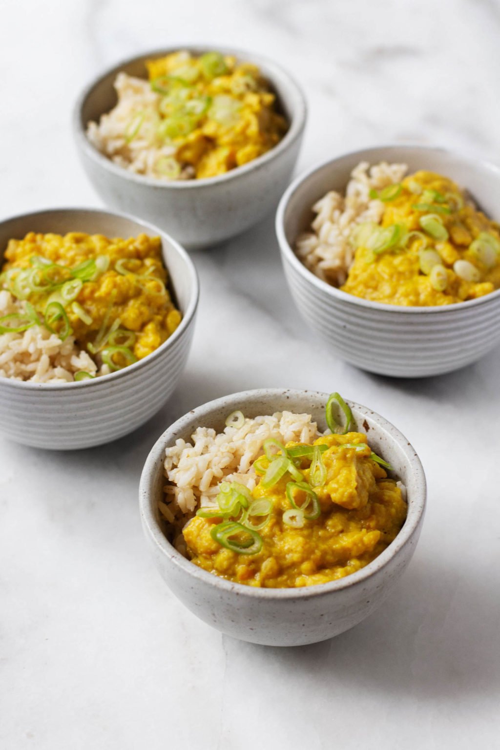 Several small bowls of a savory vegan breakfast porridge, prepared with split peas and coconut and served over rice.