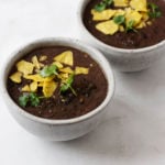 Two small bowls of a spicy vegan black bean soup, made with kale and garnished with cilantro and corn chips.