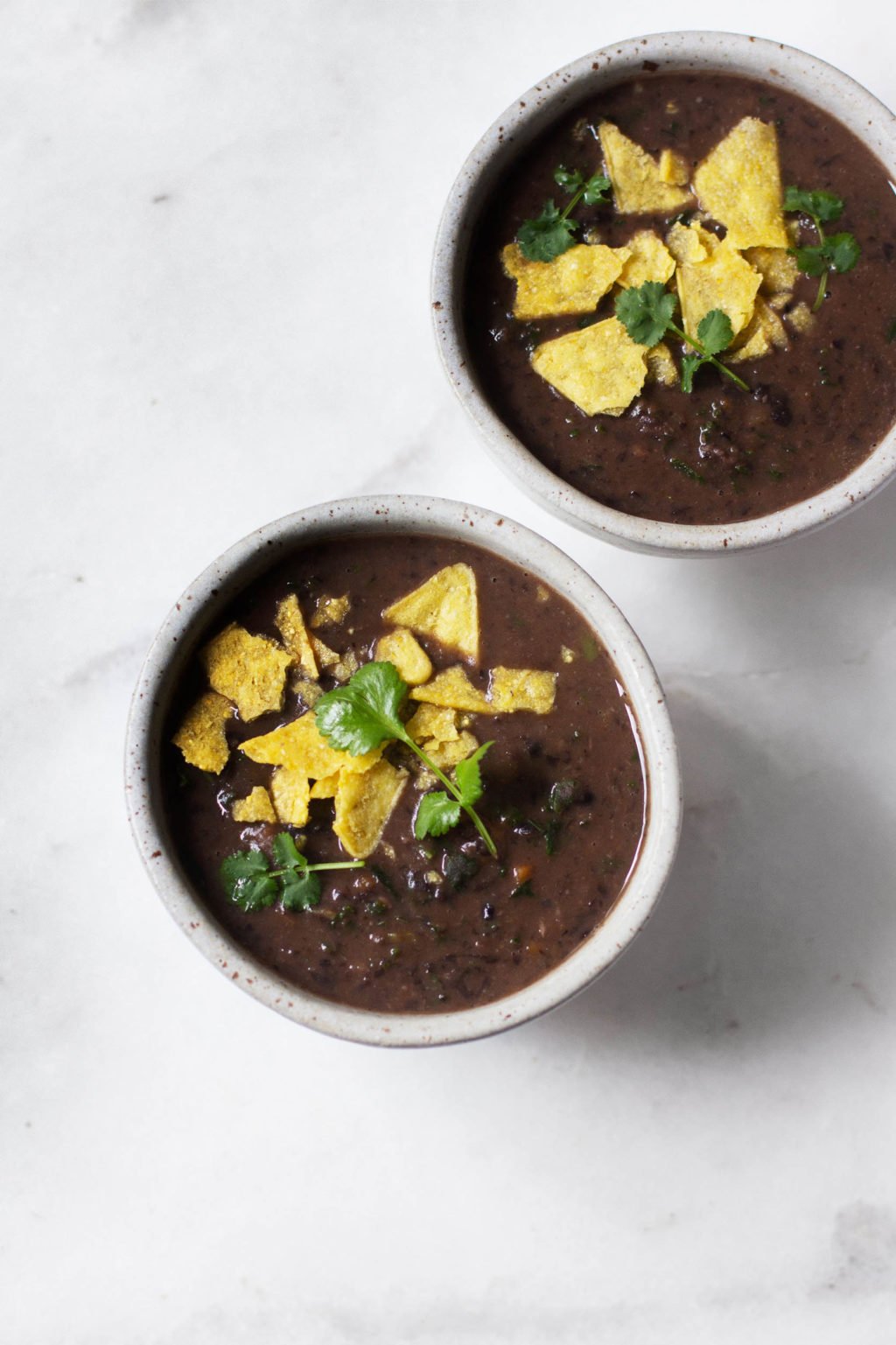 An overhead photo of two small bowls of spicy vegan black bean soup, made with kale and chipotle en adobo. 