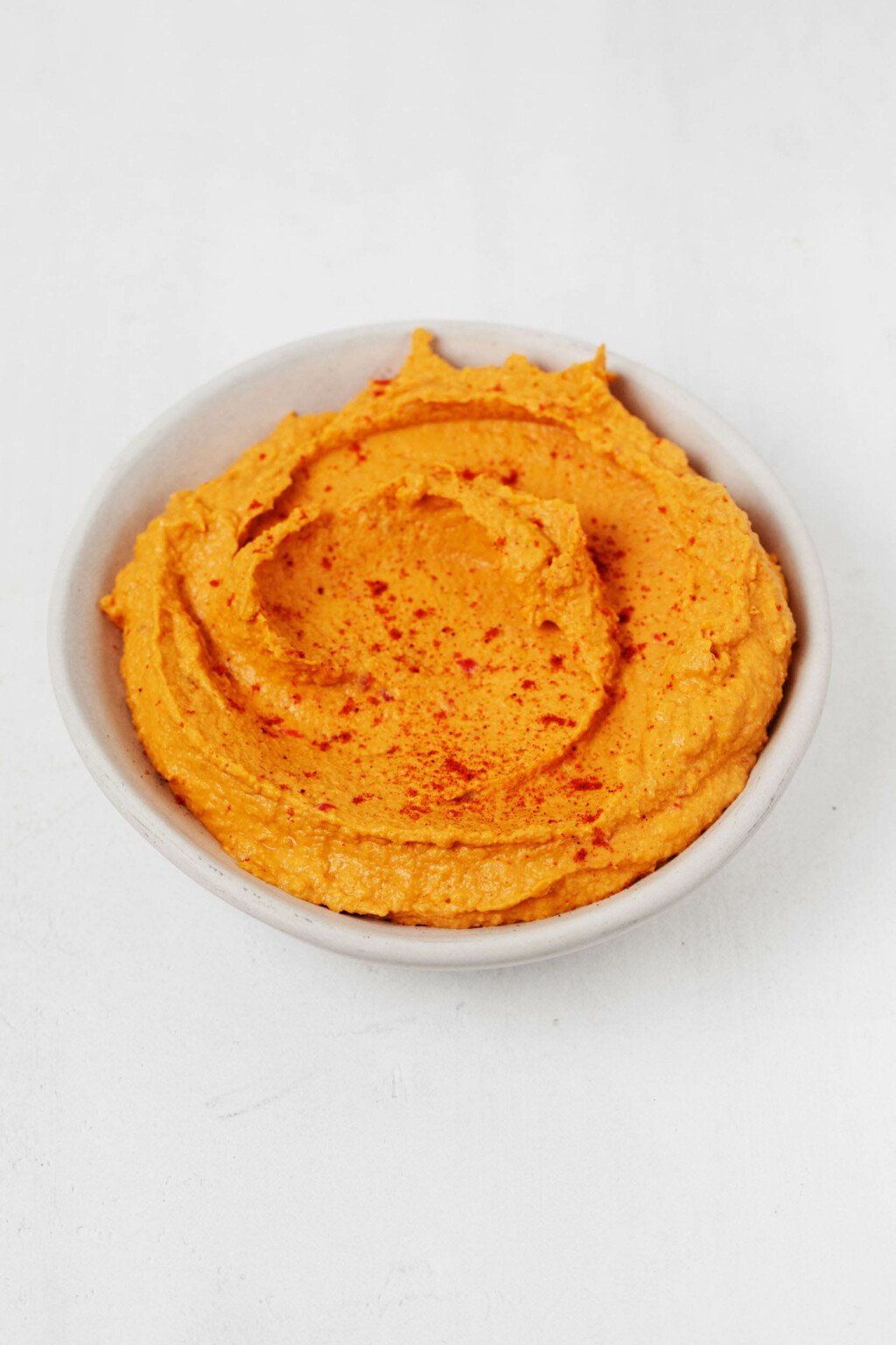 A small bowl of a dip is resting on a white surface.