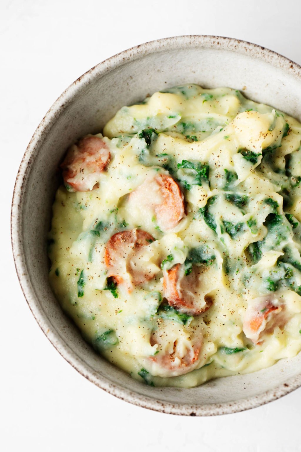 A close up image of a bowl of vegan colcannon, which has been prepared with kale and vegan sausage. 