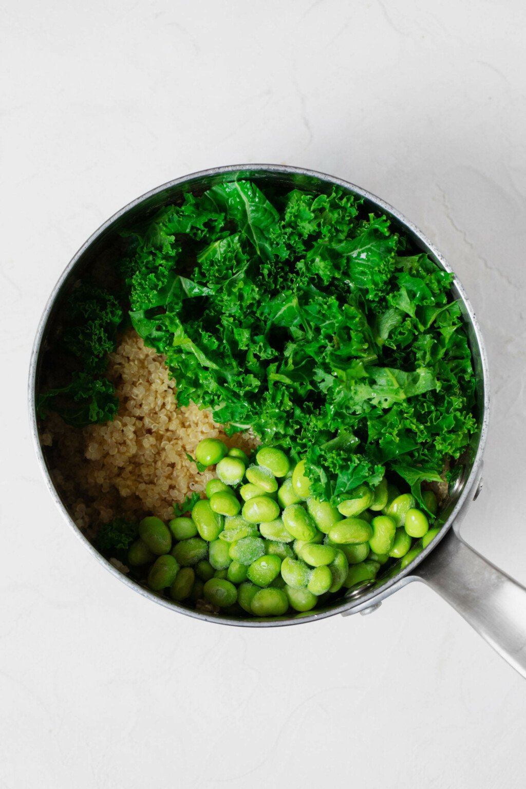 An overhead image of a silver pot, which is filled with quinoa, kale, and edamame.