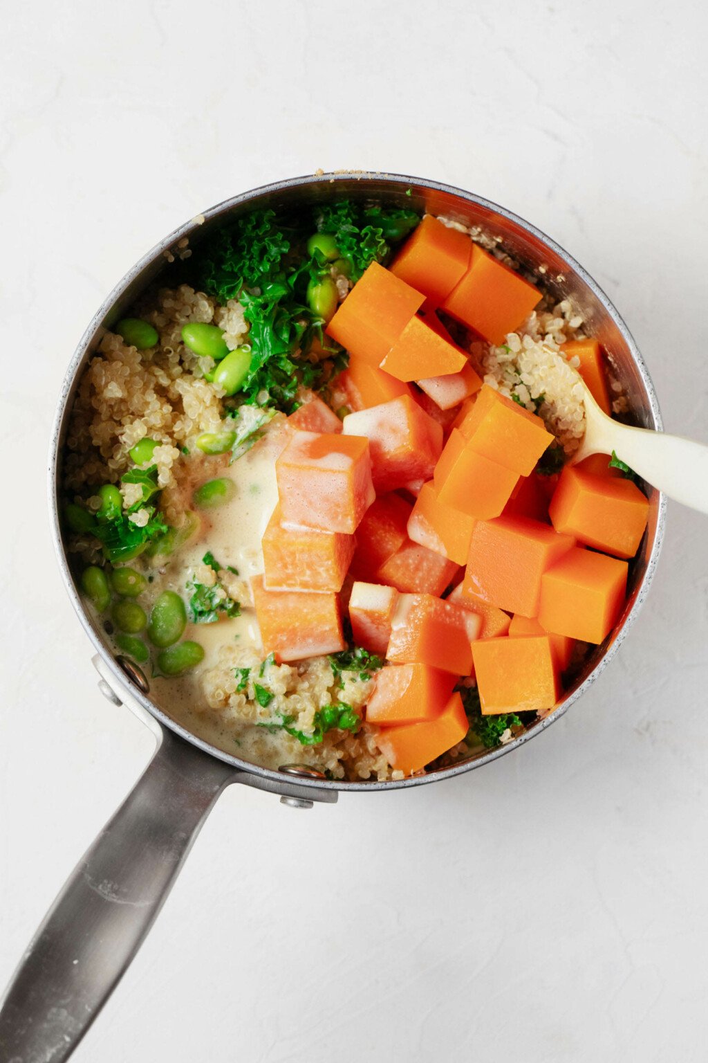 An overhead image of a silver bowl, which is filled with butternut squash, edamame, and quinoa.