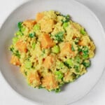 An overhead image of a round white bowl, which has been filled with a golden-hued mixture of quinoa, edamame, and butternut squash.