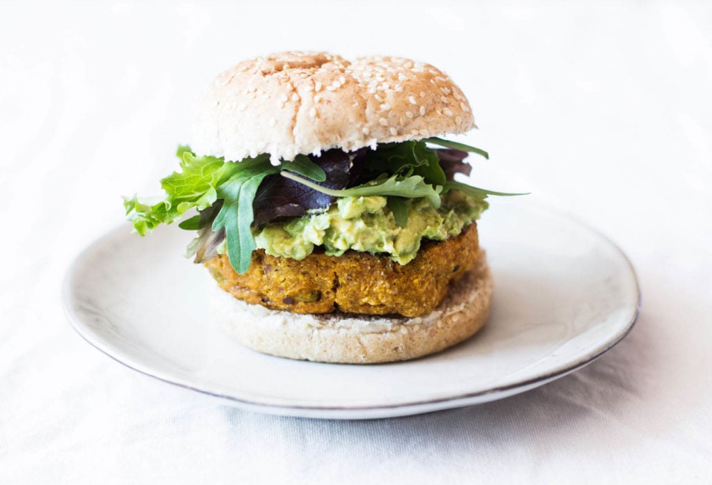 A vegan burger made with edamame and sweet potatoes is served with guacamole on a burger bun.