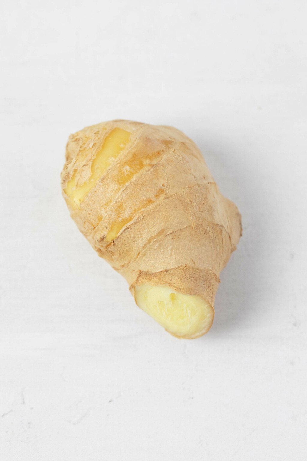 An image of a knob of ginger, resting on a white surface.