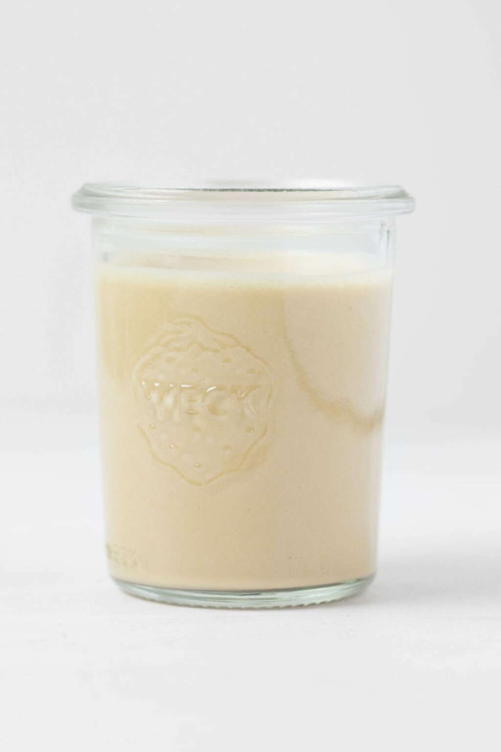 An image of a Weck mason jar, resting on a white surface, filled with a creamy miso sesame dressing.
