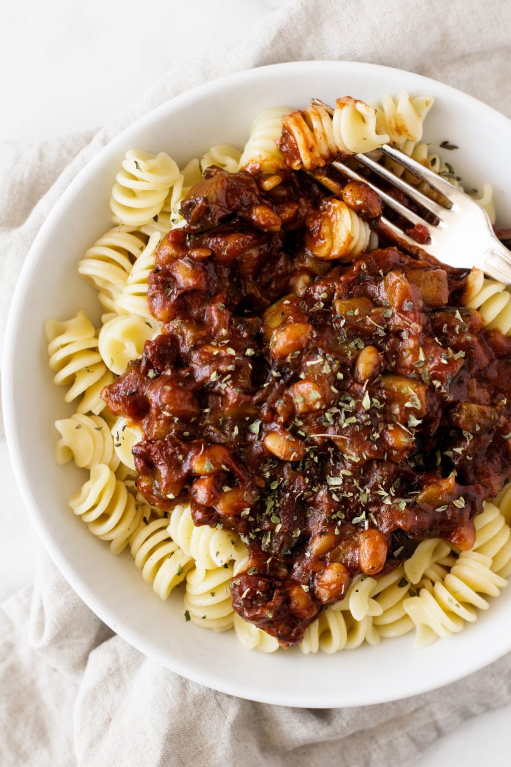 A bowl full of white bean pasta and tomato sauce rests on a linen napkin.