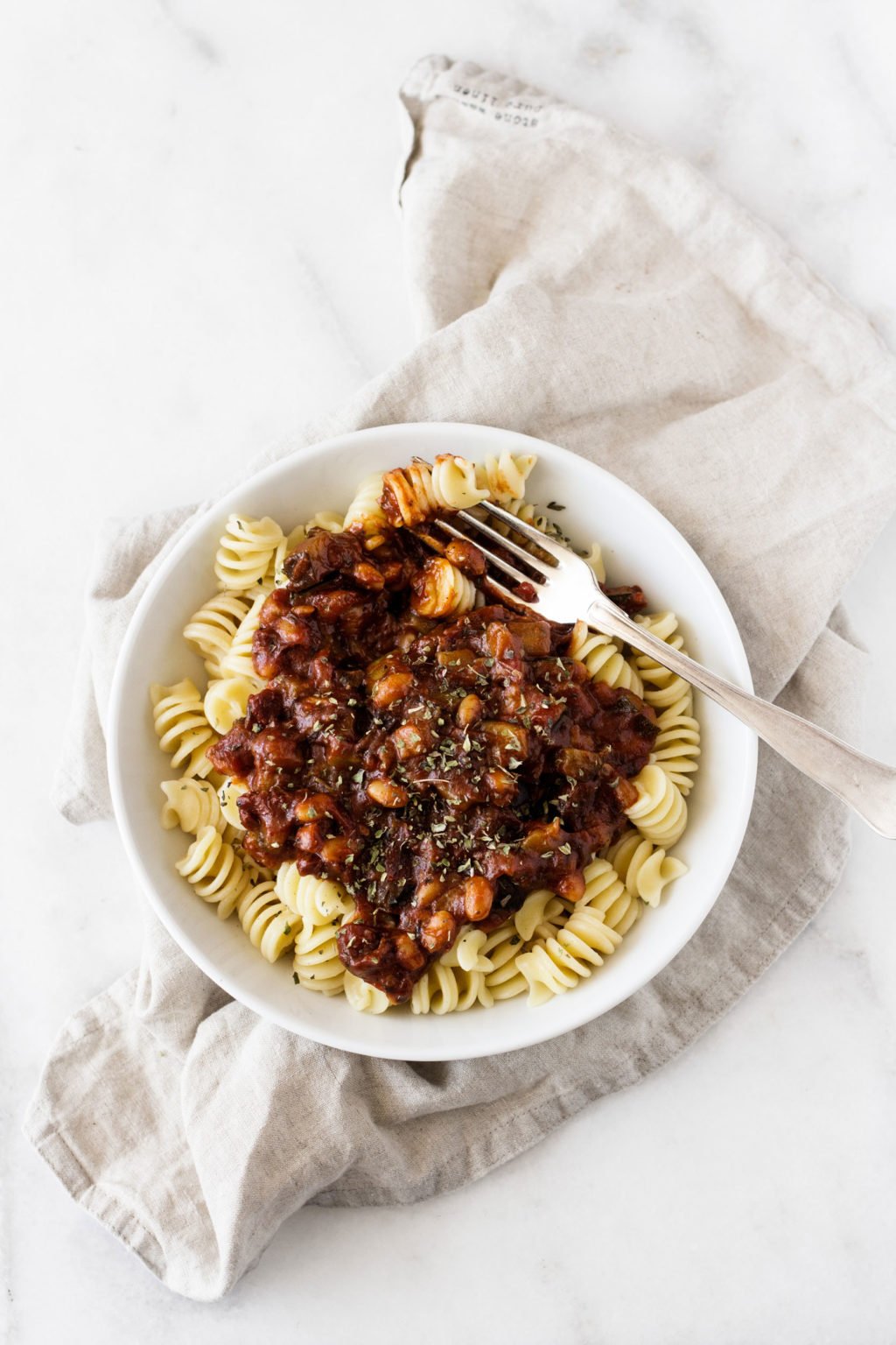 An overhead image of a bowl of fusilli with a red sauce and vegetables.