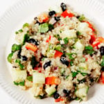 A white, fluted plate is piled with a colorful salad of quinoa, black beans, and assorted diced vegetables.