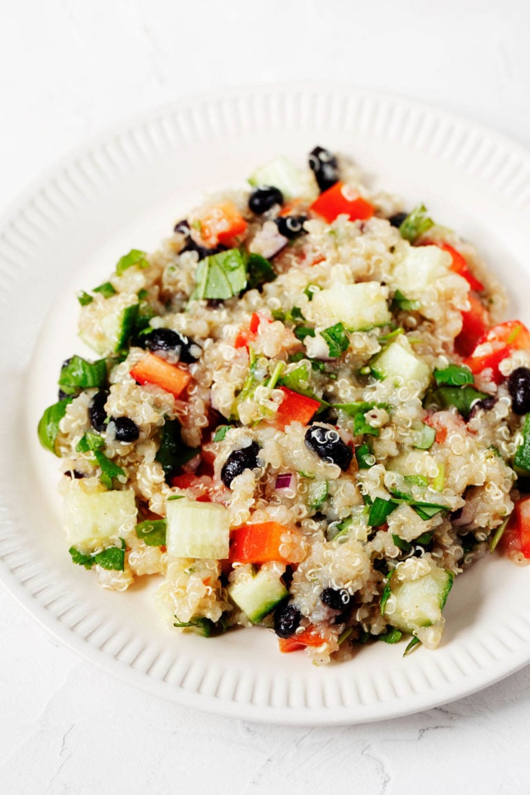 A white, fluted plate is piled with a colorful salad of quinoa, black beans, and assorted diced vegetables.