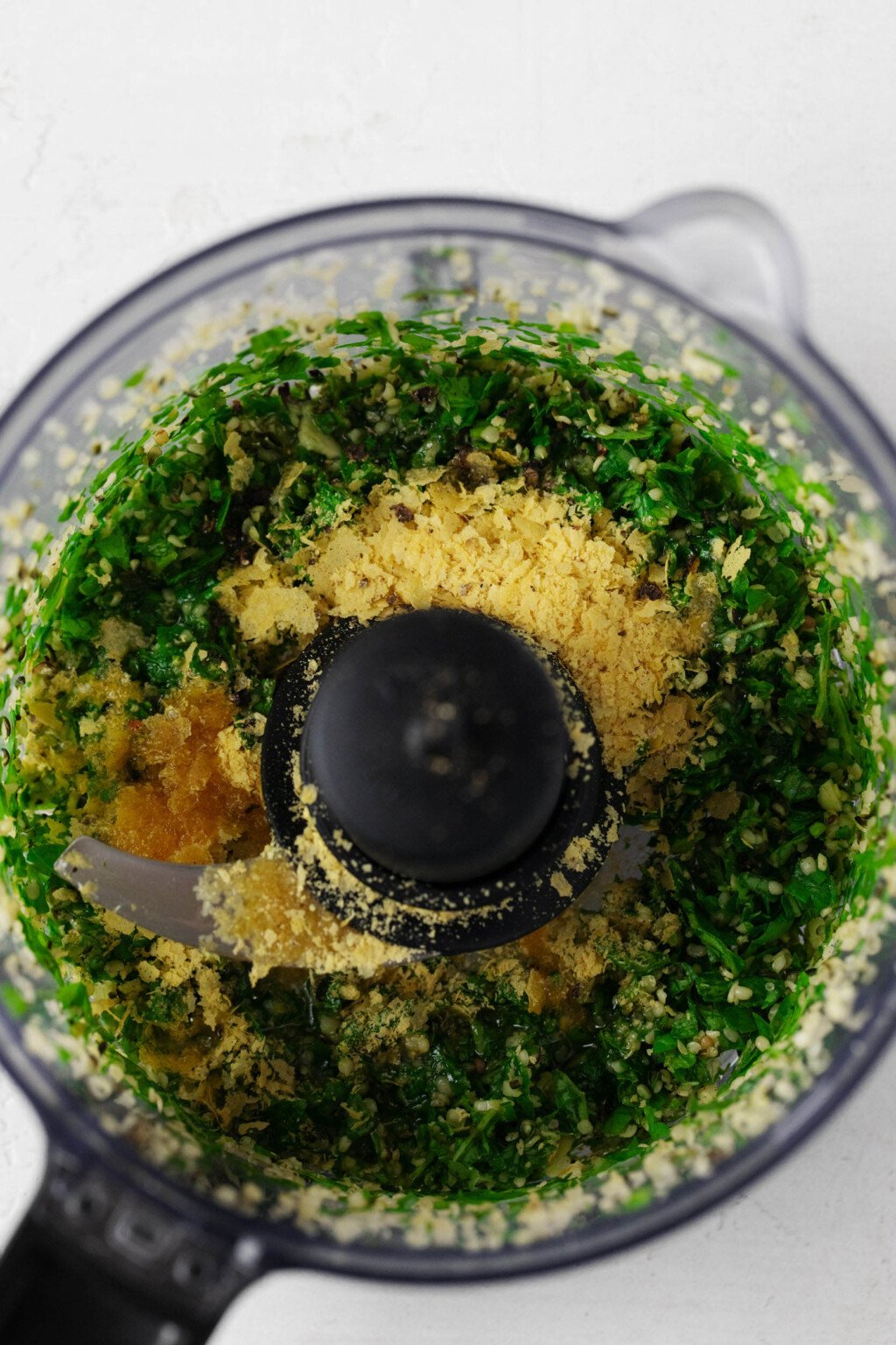 A closeup, overhead image of the bowl of a food processor that is being used to make basil pesto sauce.