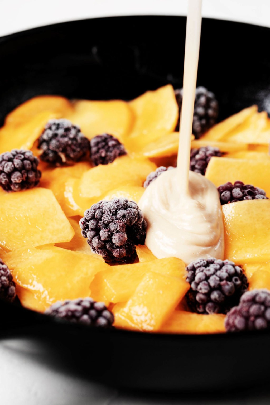 Cake batter is being poured over frozen fruit in a cooking vessel.