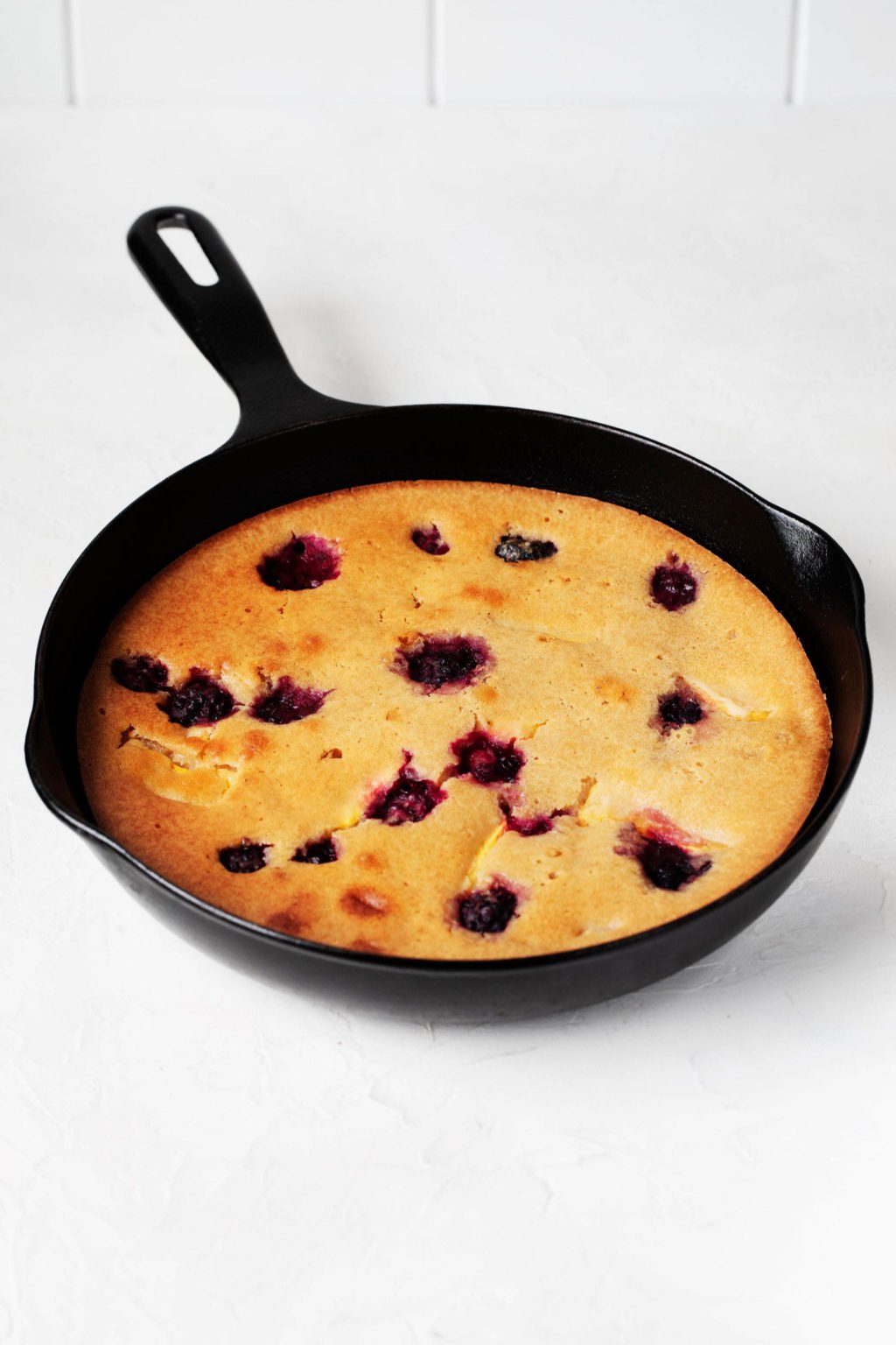 A black, cast iron skillet is filled with a vegan peach blackberry cake. 