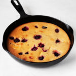 A black, cast iron skillet is filled with a vegan peach blackberry cake.