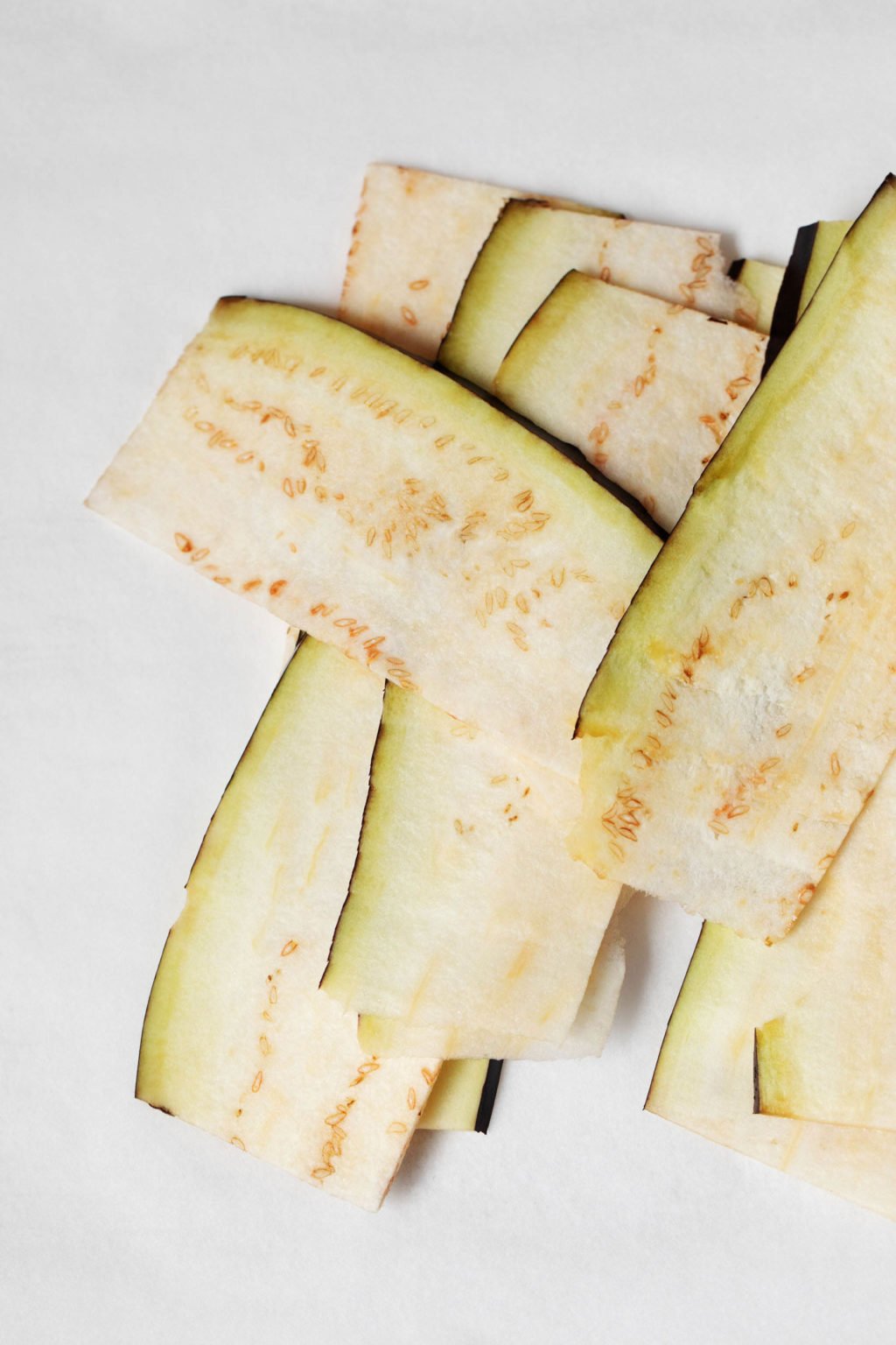 Very thin slices of eggplant are laid out on a white surface.