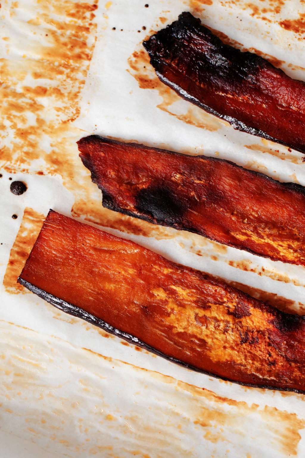 An overhead images of a few strips of eggplant, which have been recently baked in the oven on white parchment.