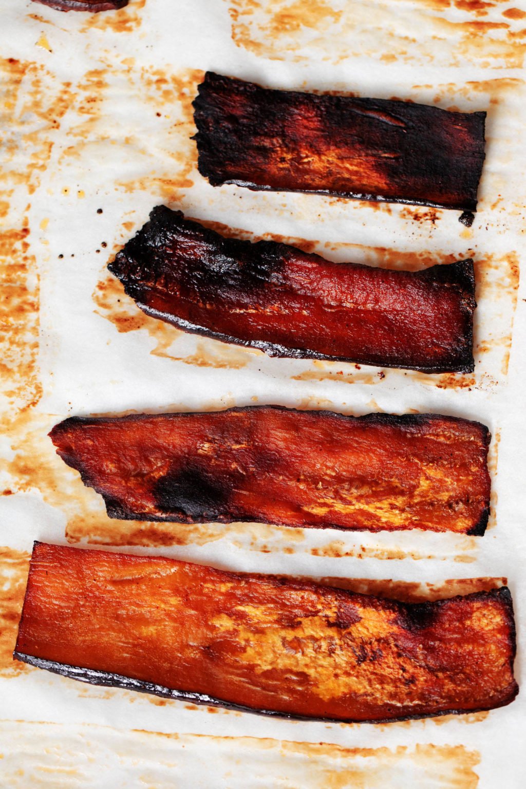 Very thin slices of vegan eggplant bacon are laid out on a parchment lined baking sheet. 