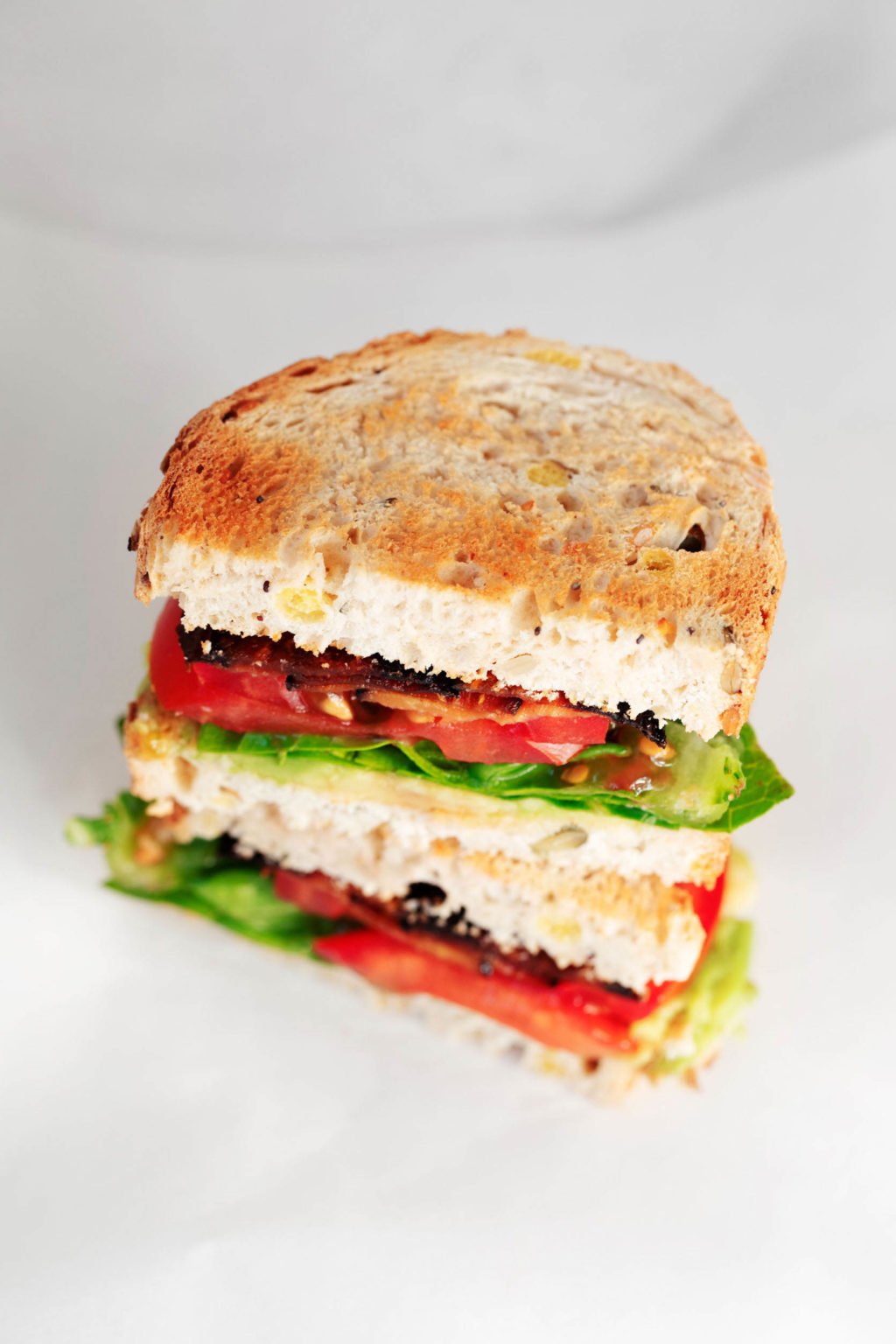 An angled, overhead image of a plant-based sandwich on white bread, with lettuce, tomato, and marinated eggplant slices.