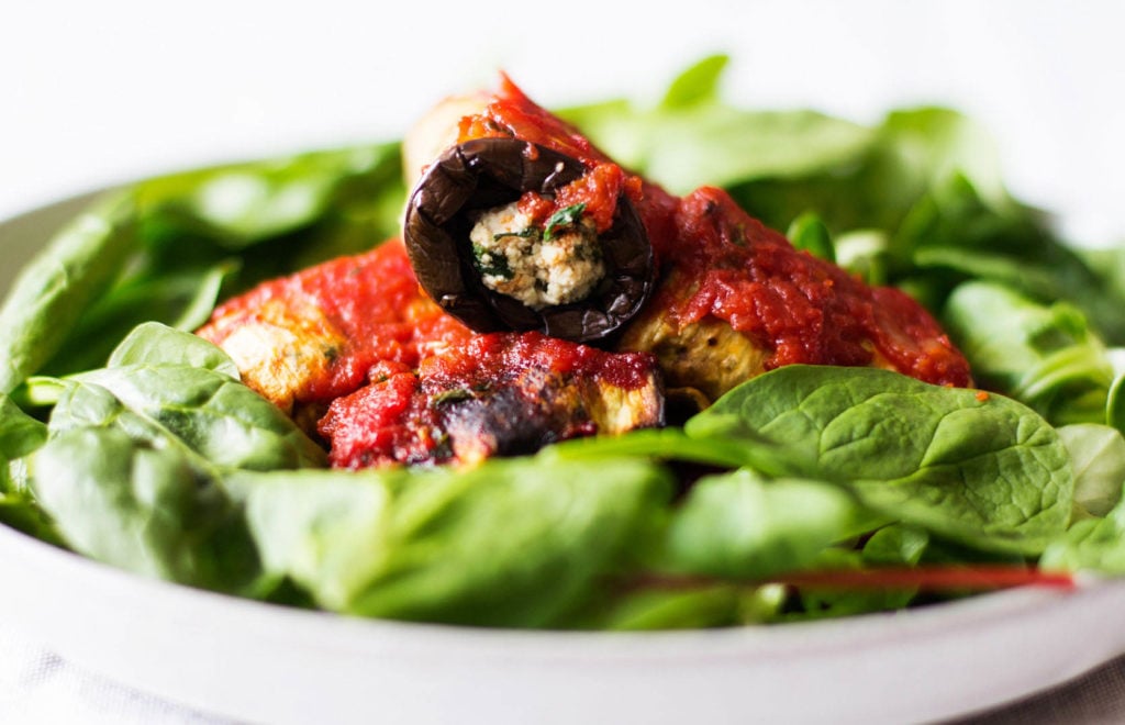 A vegan eggplant rollatini rests on a bed of green baby spinach.