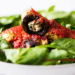 A vegan eggplant rollatini rests on a bed of green baby spinach.