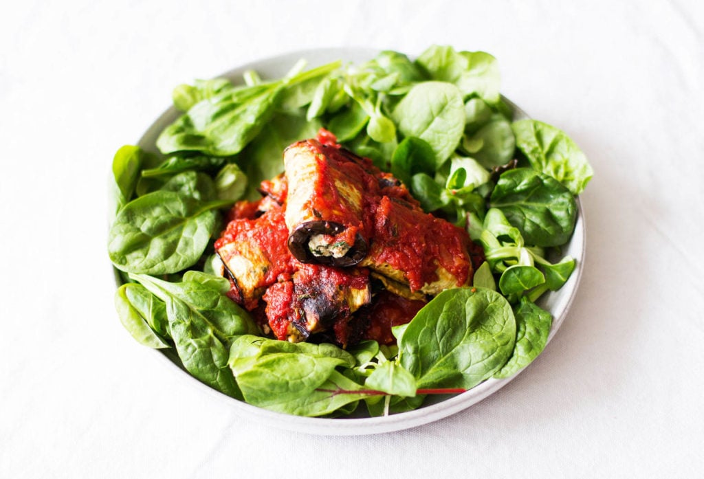 A white plate of green spinach is covered with baked vegetables and marinara.