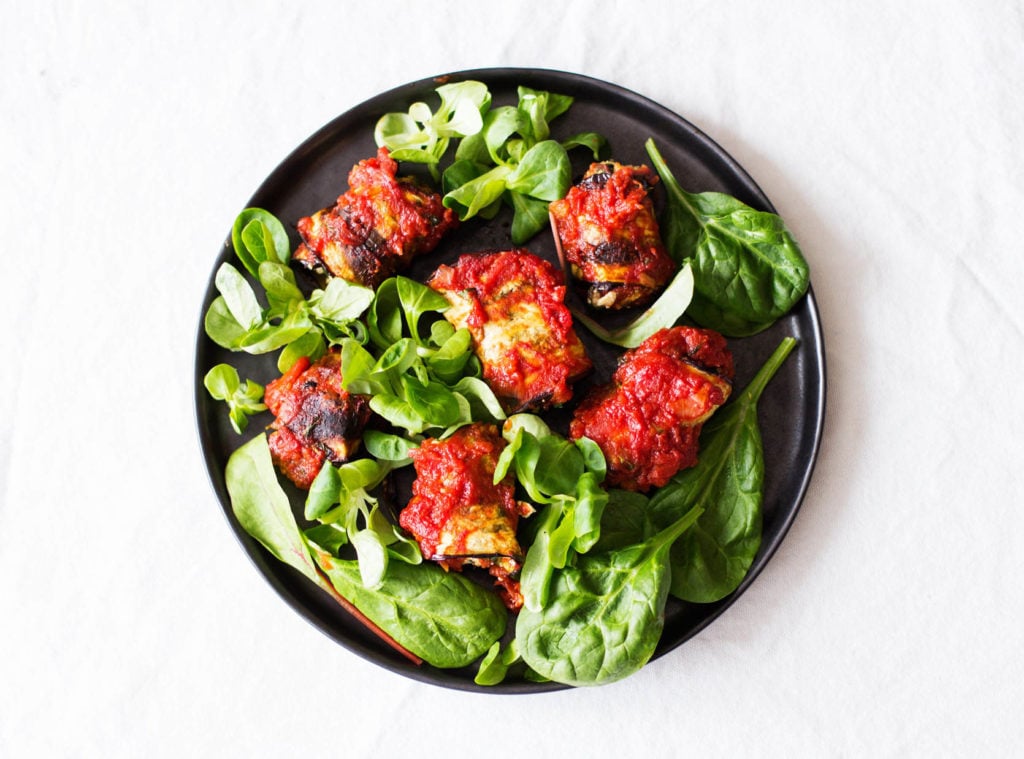 An overhead image of eggplant rolls, which have been covered in marinara sauce and served with spinach.