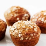 An angled photograph of freshly baked banana oat chia muffins, sprinkled with fresh rolled oats.