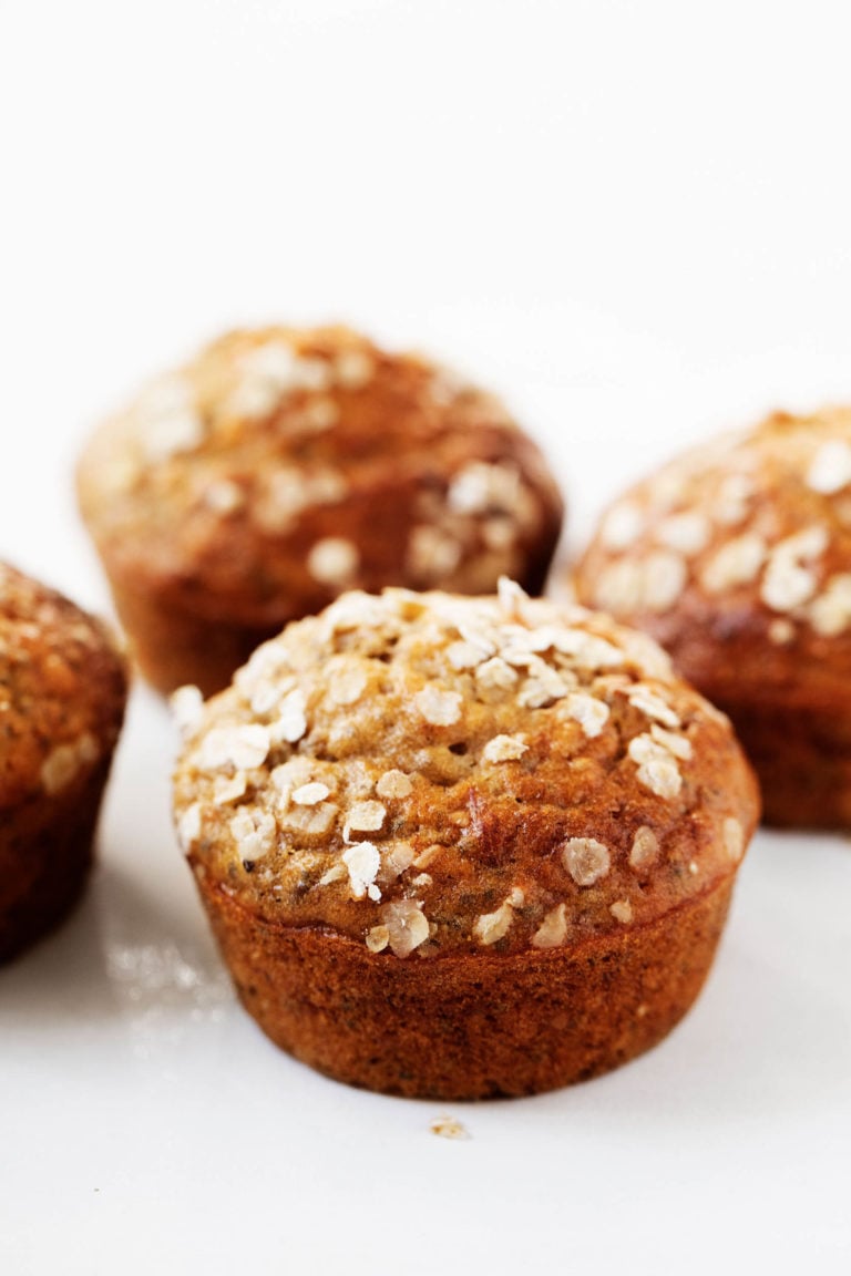 An angled photograph of freshly baked banana oat chia muffins, sprinkled with fresh rolled oats.