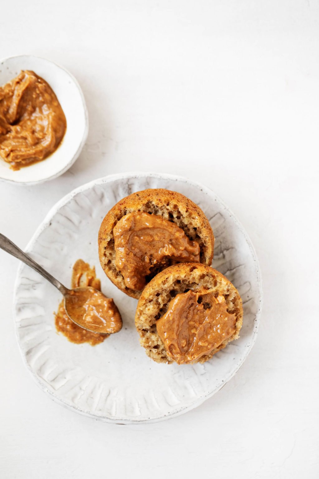 A vegan banana muffin spread with chunky peanut butter, laid out on a serving plate.