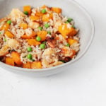 A white, ceramic bowl holds a mixture of roasted butternut squash, rice, and peas.