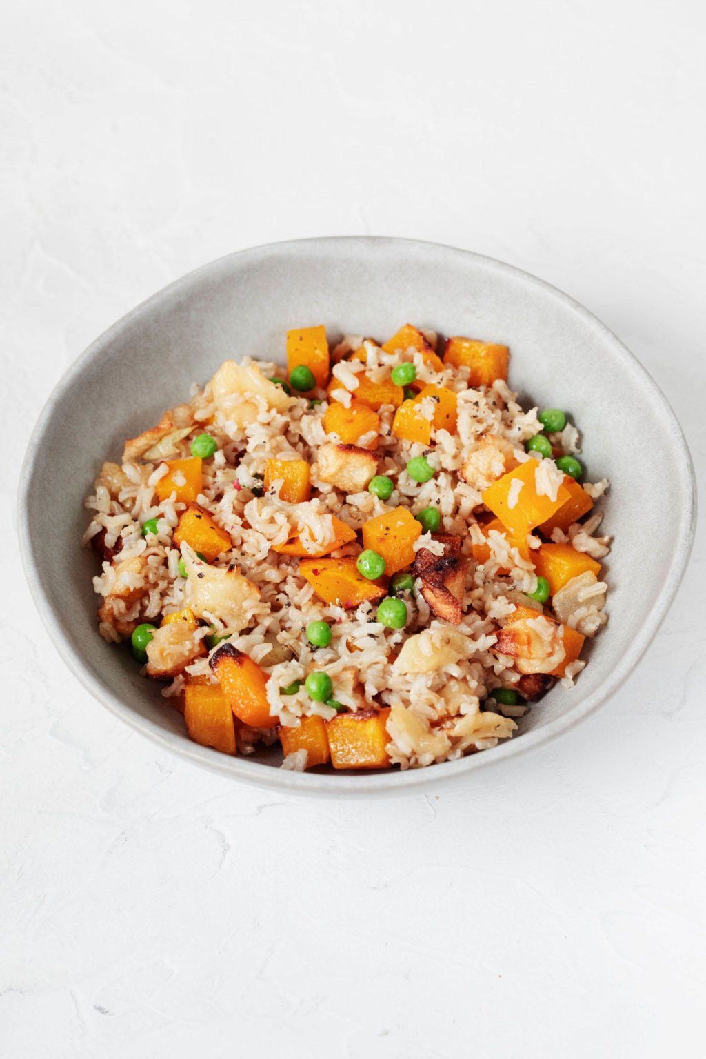 An autumnal whole grain and vegetable dish rests in a light white and gray ceramic bowl. 