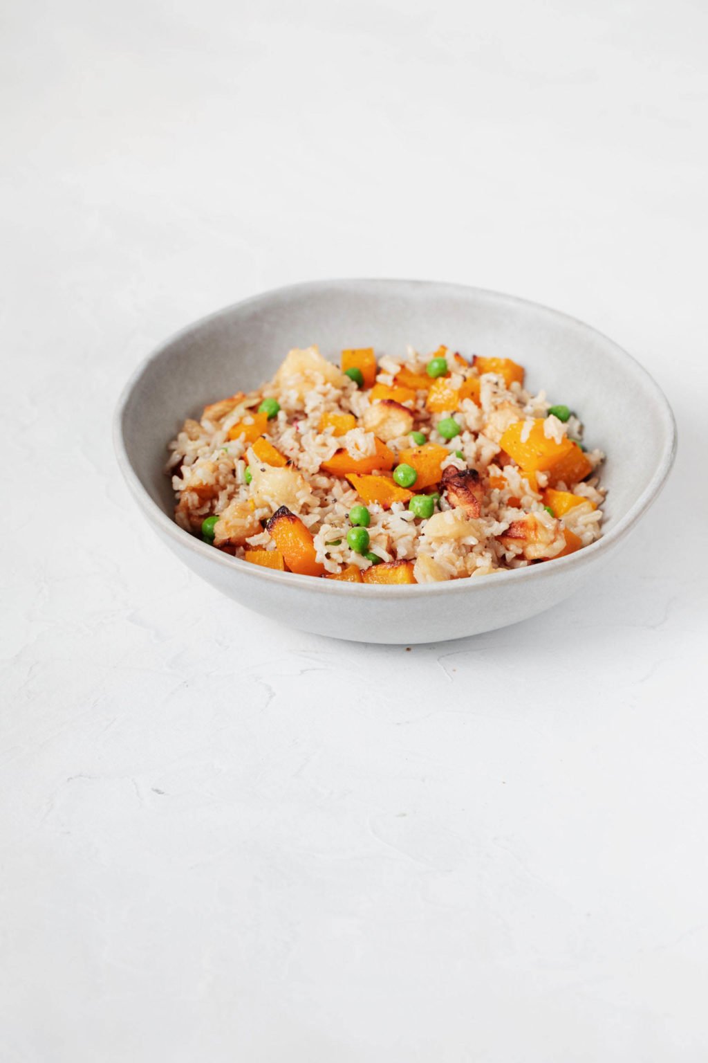 An angled image of a round, white ceramic bowl filled with rice and roasted autumn vegetables.